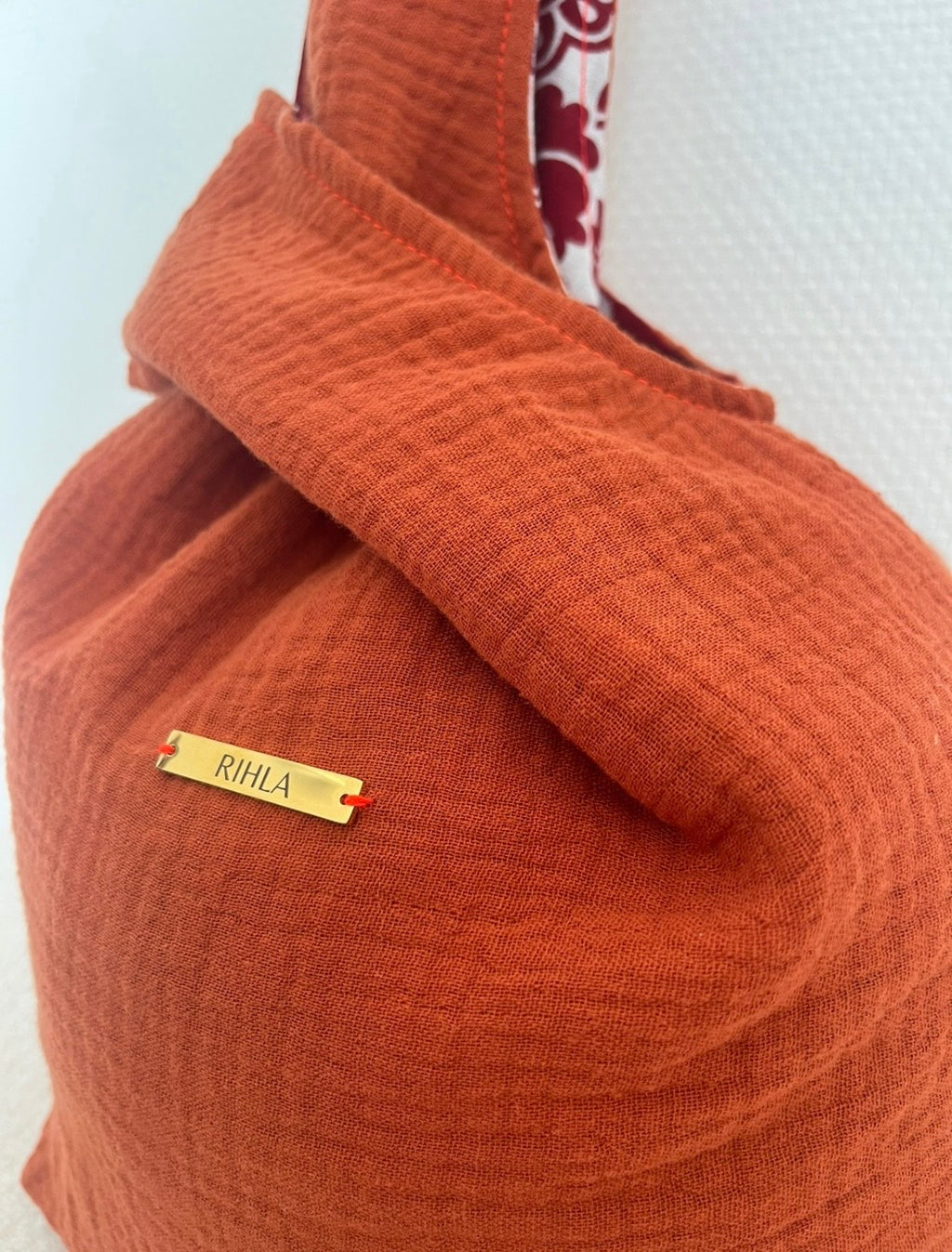 Sac Rihla fait main en gaze de coton orange et tissu comorien rouge, modèle réversible style knot bag porté à la main.