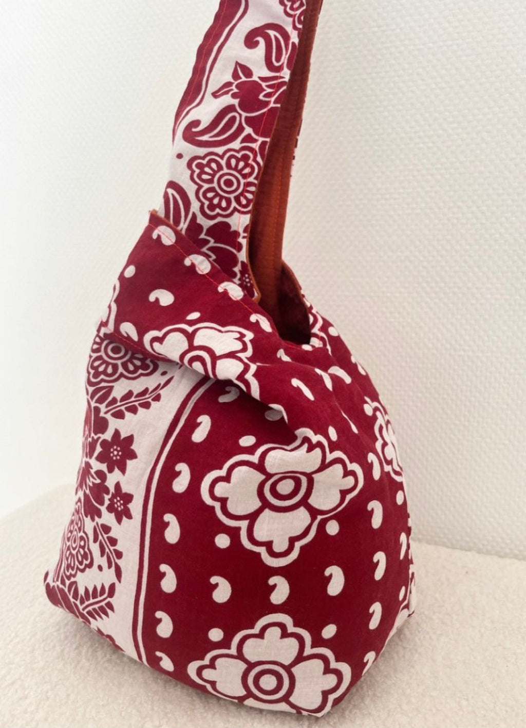 Sac Rihla fait main en gaze de coton orange et tissu comorien rouge, modèle réversible style knot bag porté à la main.
