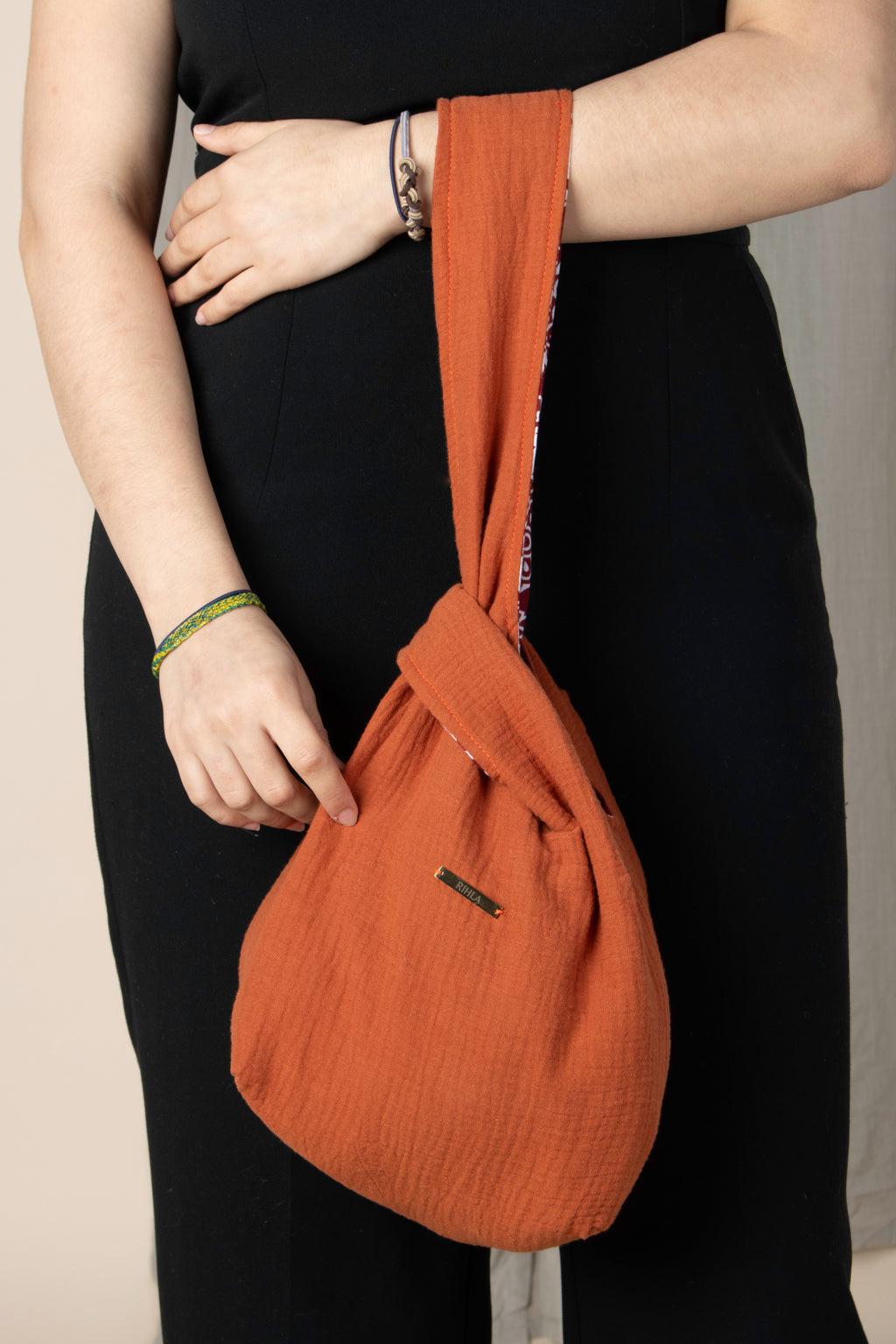 Sac Rihla fait main en gaze de coton orange et tissu comorien rouge, modèle réversible style knot bag porté à la main.